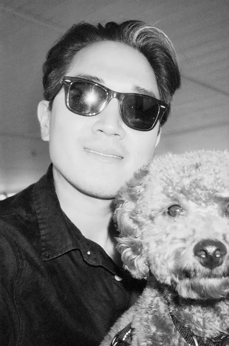 Jason in sunglasses with Toby, a curly-haired dog, shot on black and white film