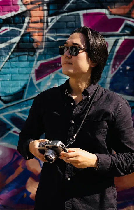 Jason holding a small film camera in front of a graffiti wall