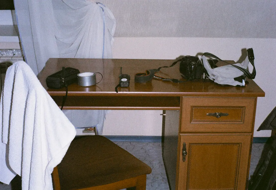 A wooden desk shot on expired film, with a camera bag, a light meter and a strap set down on it